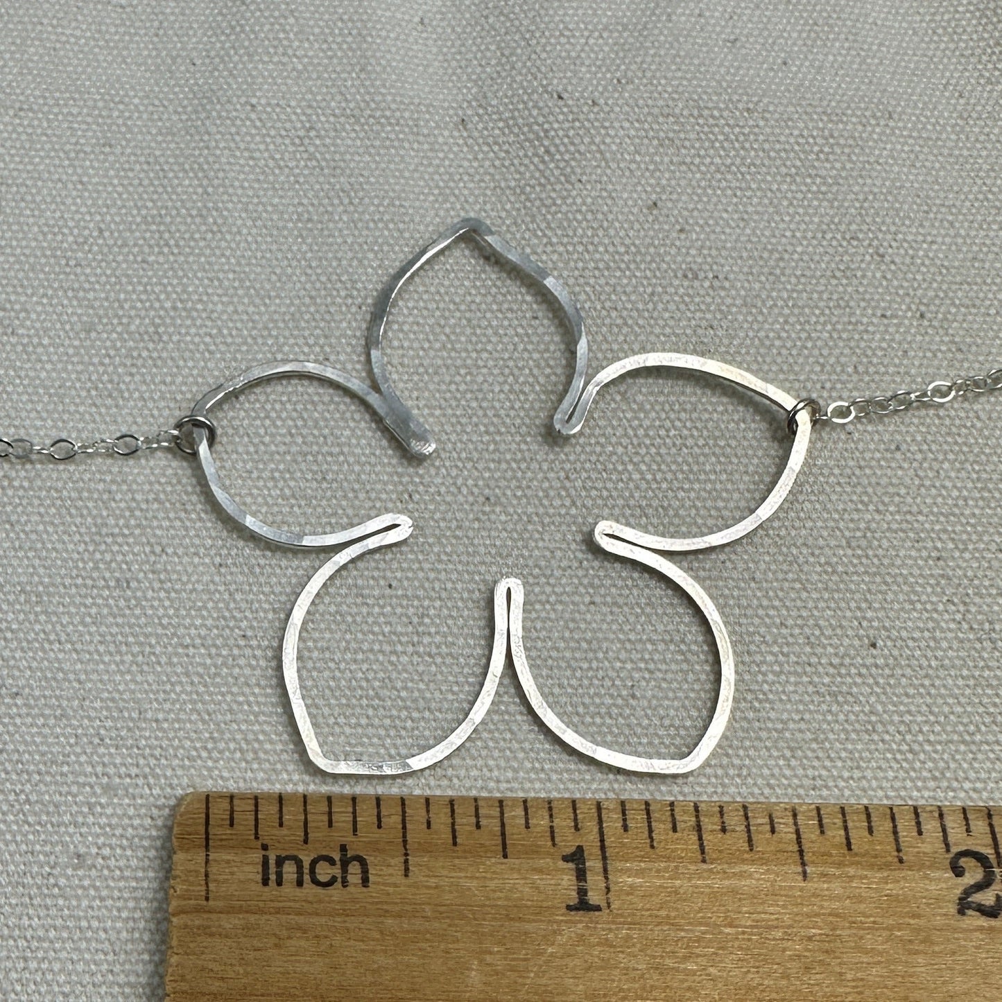 Silver flower-shaped pendant on a chain with a ruler for scale on a gray background