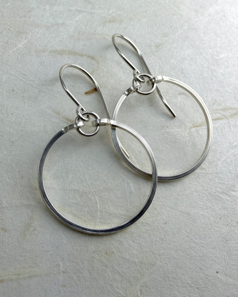 Pair of silver circle earrings on a light gray surface