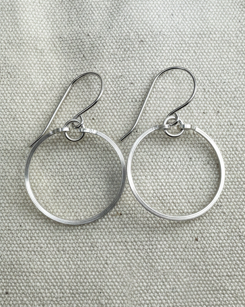 Pair of silver circle earrings on a textured  fabric background