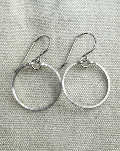 Pair of silver circle earrings on a textured  fabric background