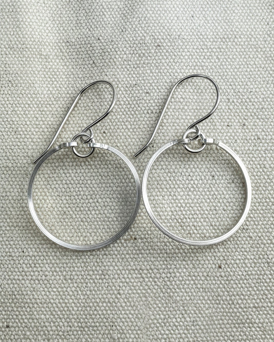 Pair of silver circle earrings on a textured  fabric background