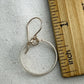 gold circle earring on a gray fabric background with a wooden ruler for scale.
