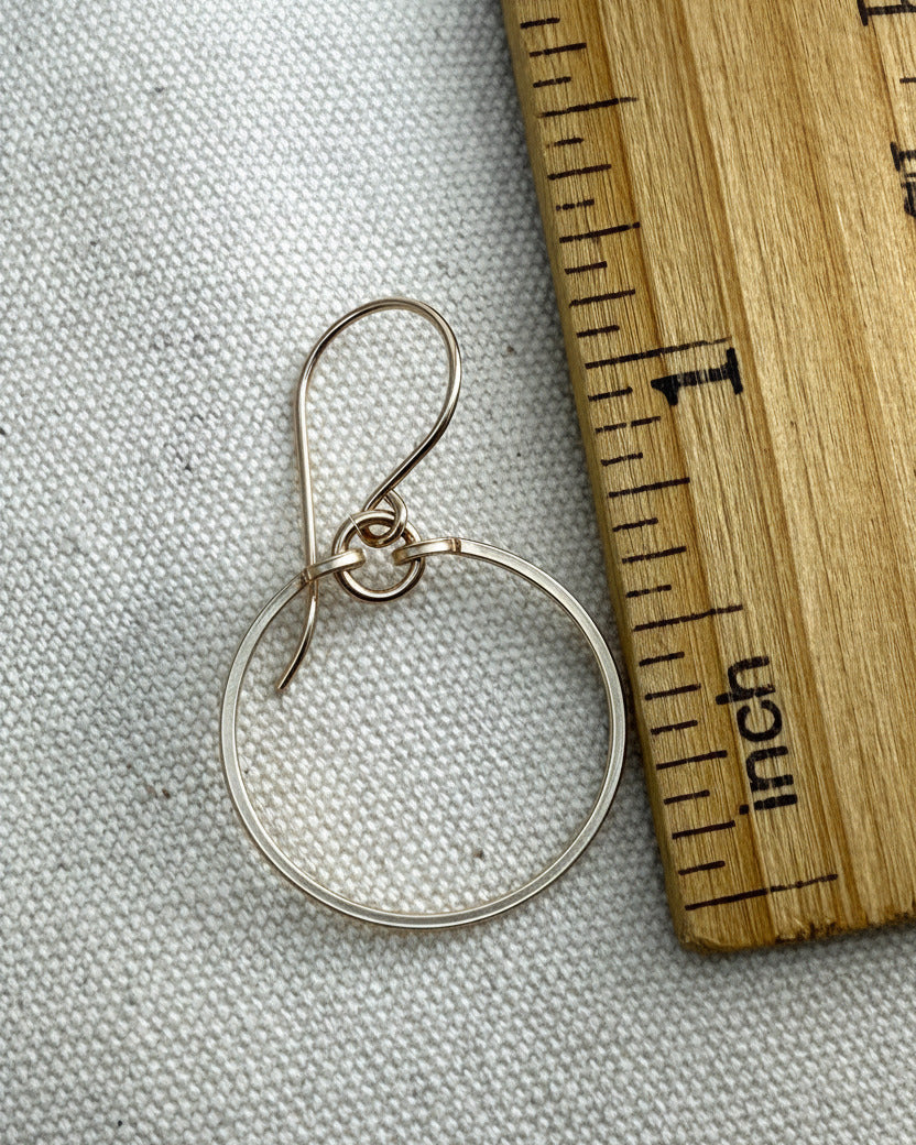 gold circle earring on a gray fabric background with a wooden ruler for scale.