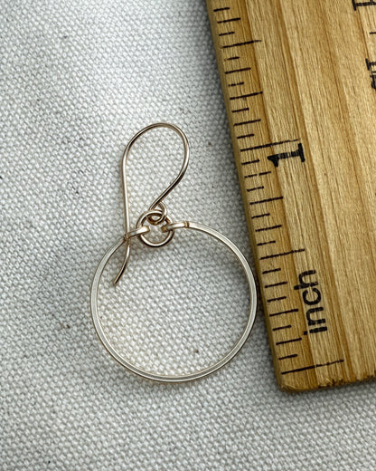 gold circle earring on a gray fabric background with a wooden ruler for scale.