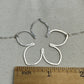 Silver flower-shaped pendant on a chain with a ruler for scale on a gray background
