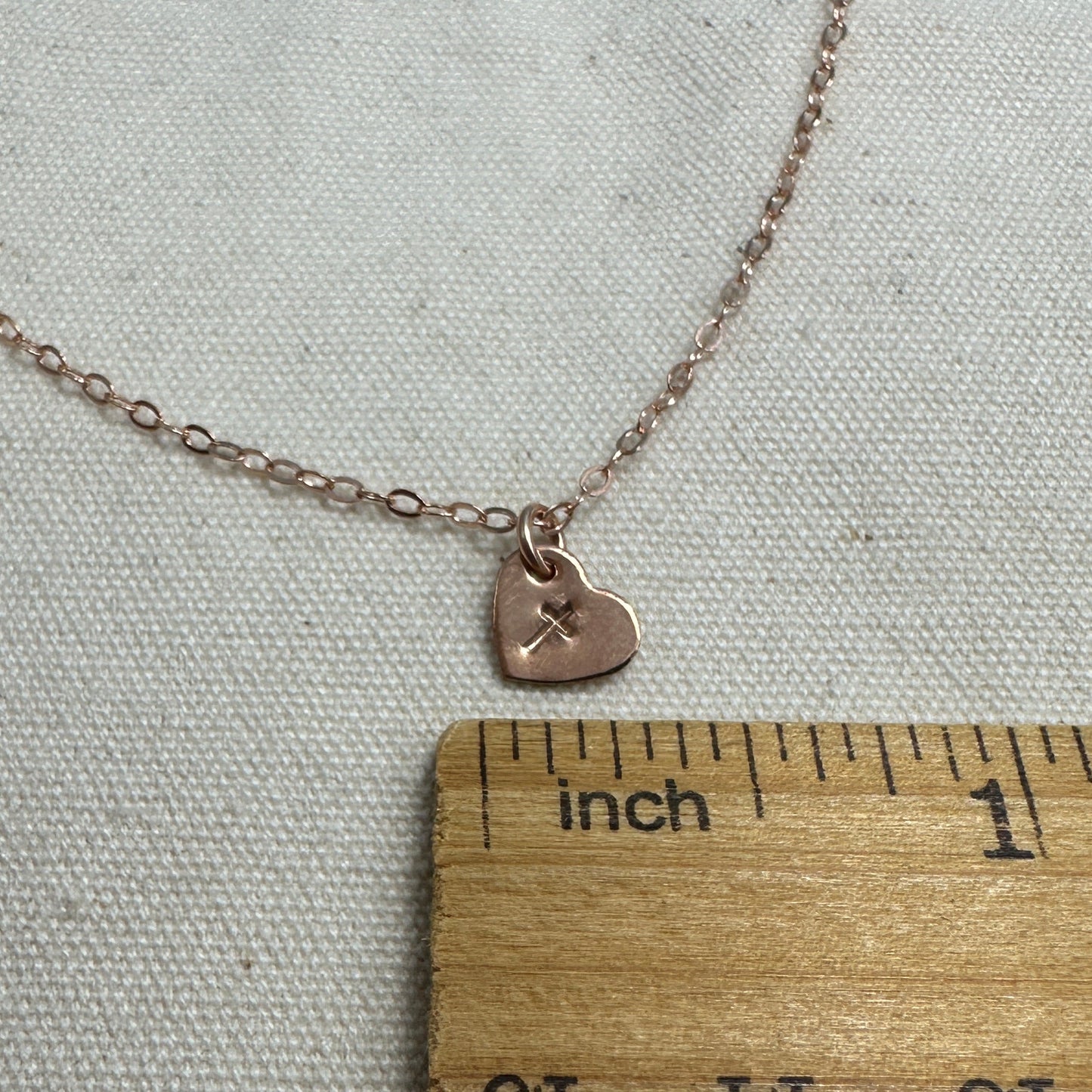 Necklace with a heart pendant next to a wooden ruler on a textured surface