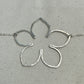 Silver flower-shaped pendant on a chain with a ruler for scale on a gray background