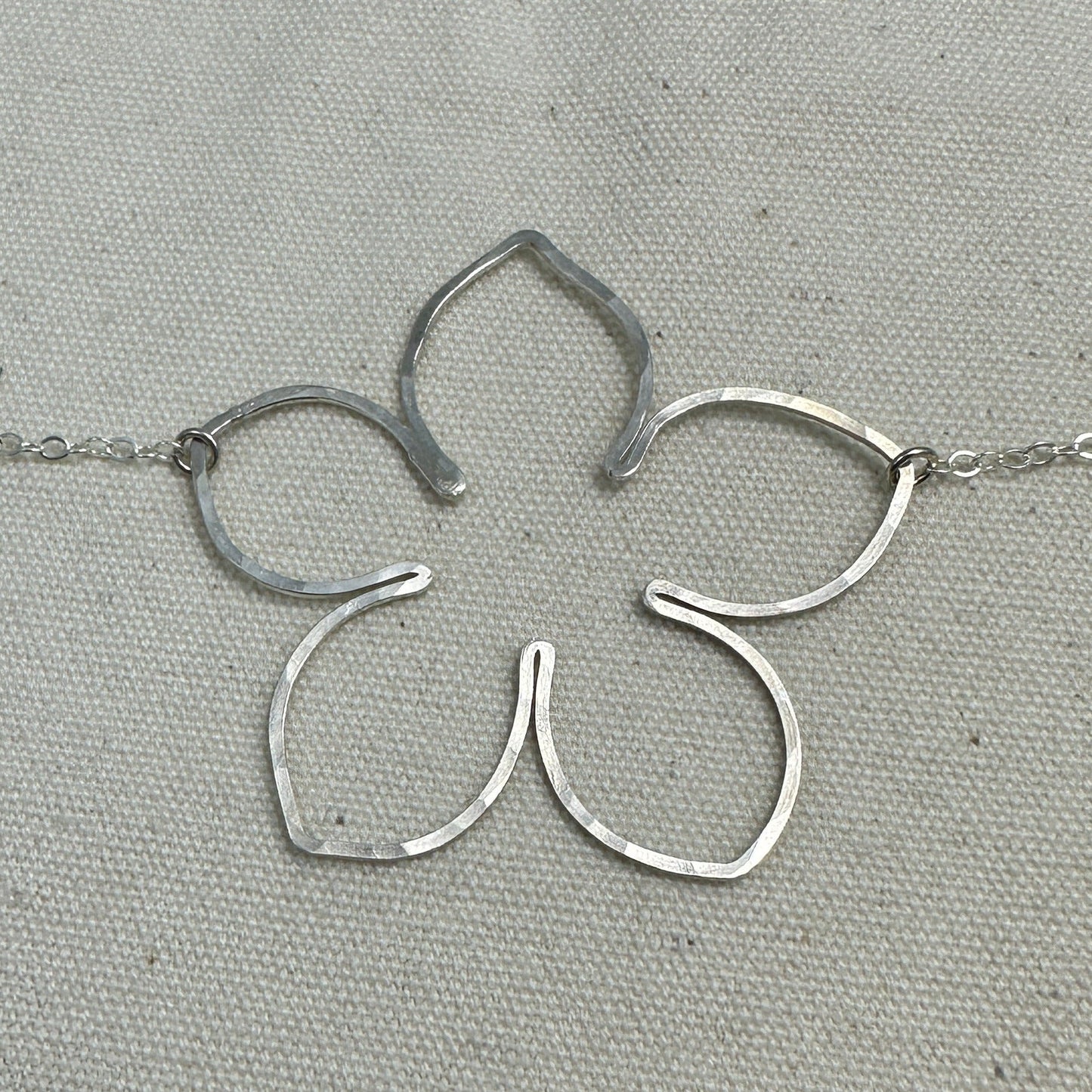 Silver flower-shaped pendant on a chain with a ruler for scale on a gray background