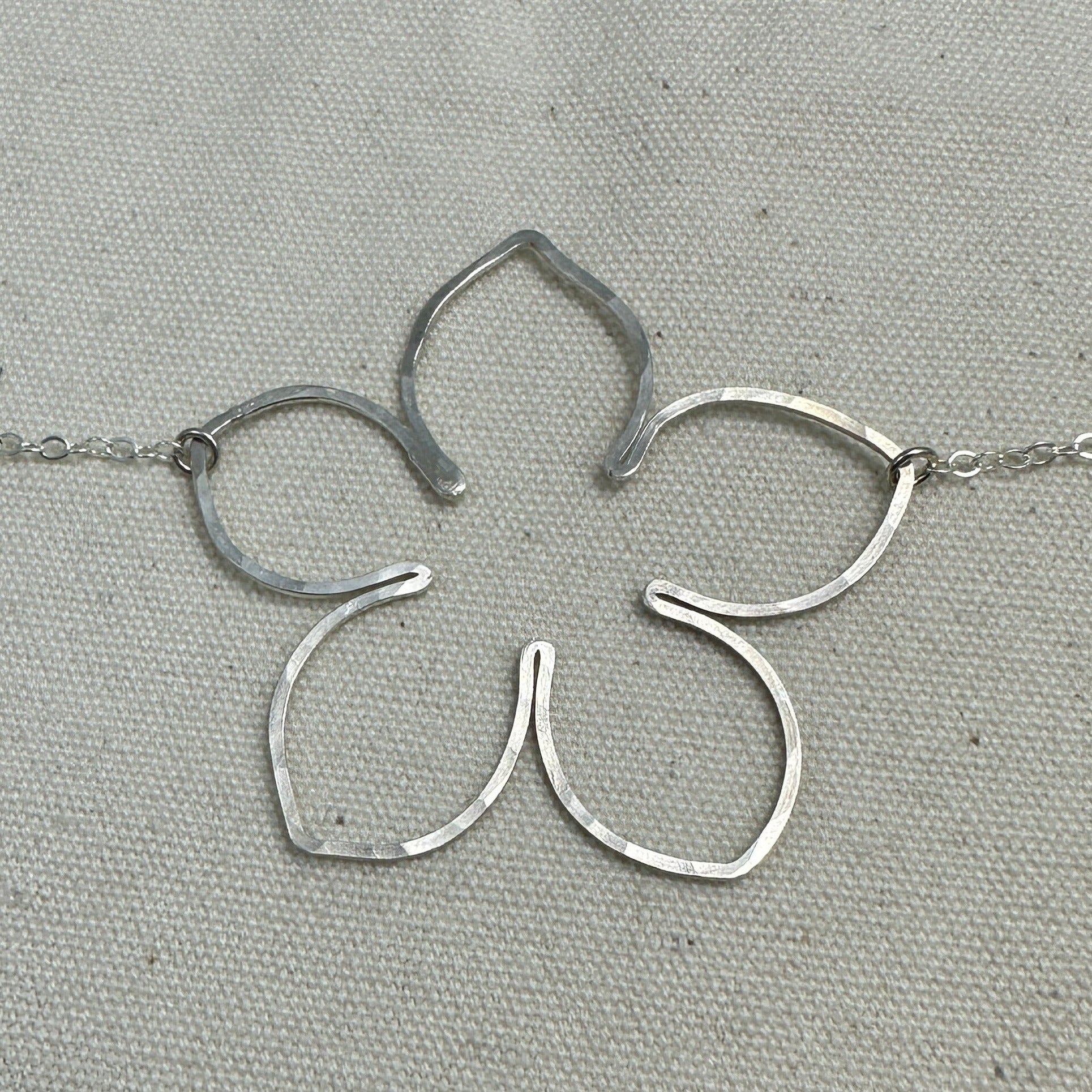 Silver flower-shaped pendant on a chain with a ruler for scale on a gray background