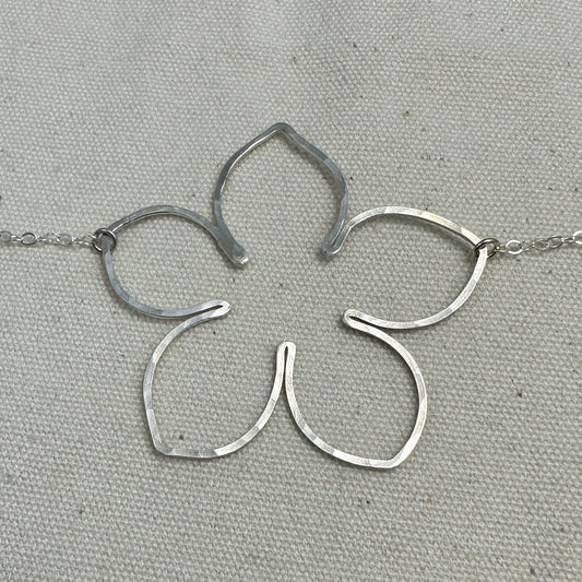 Silver flower-shaped pendant on a chain with a ruler for scale on a gray background