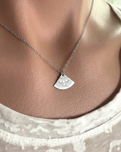 silver necklace with a unique pendant worn by a person against a neutral background