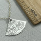 silver necklace with a decorative pendant on a gray surface next to a wooden ruler.