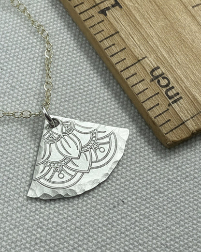 silver necklace with a decorative pendant on a gray surface next to a wooden ruler.