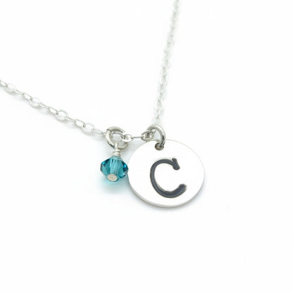 A sterling silver necklace with a large initial letter 'C' charm and a small birthstone crystal pendant.