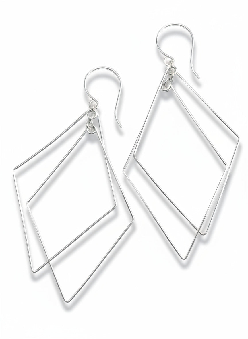 Pair of silver geometric earrings on a textured beige background